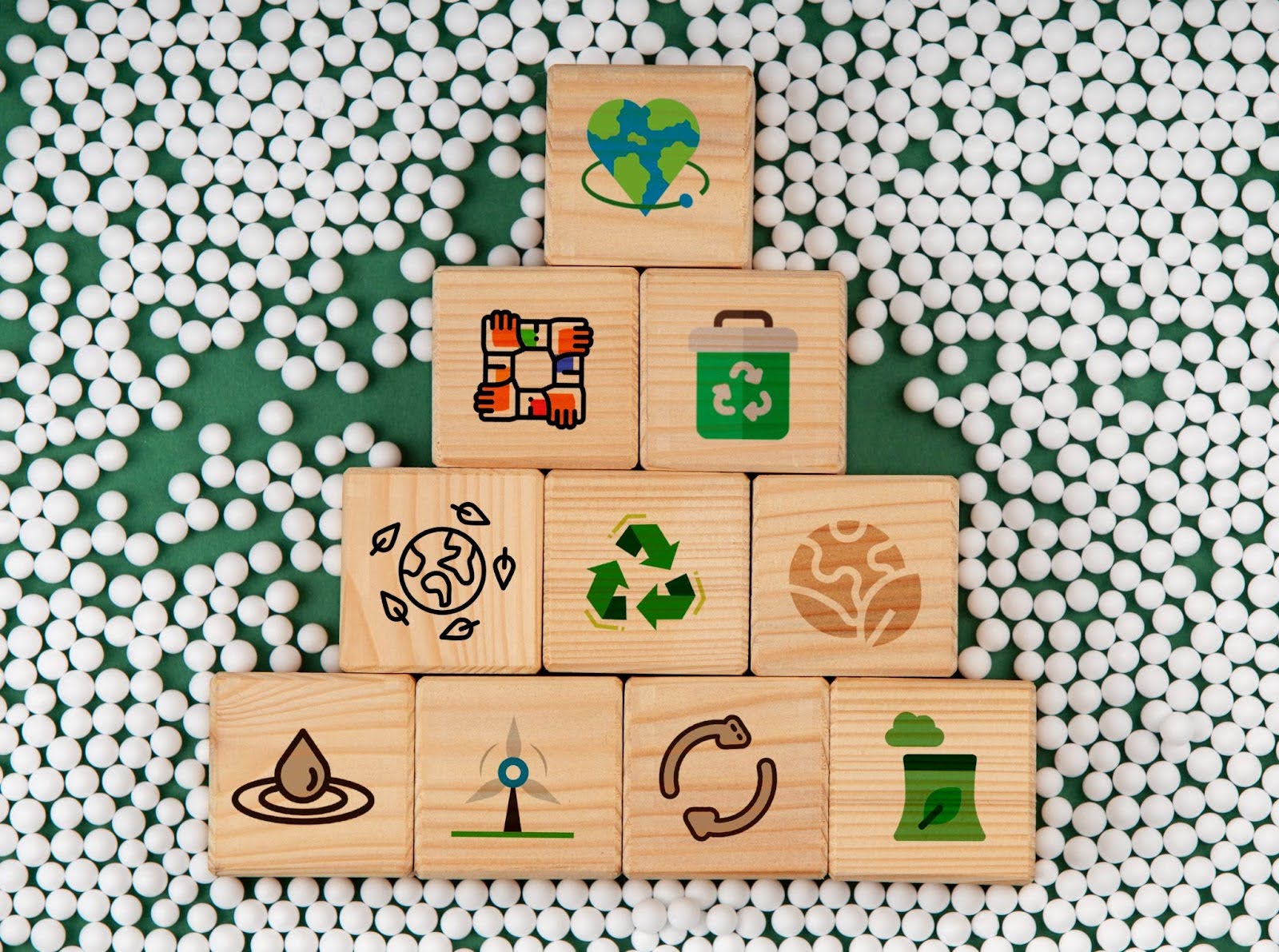 Wooden block pyramid with eco icons: heart-globe at top; lower show hands, recycle bin, globe, water droplet, energy icons.
