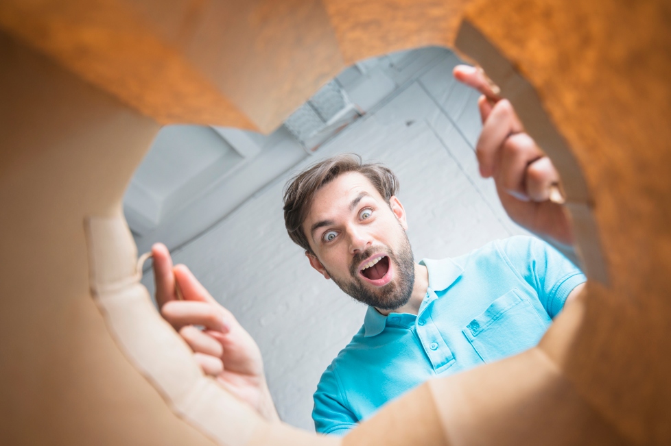 Low angle view of a surprised man in a blue shirt looking inside a paper bag with excitement and amazement