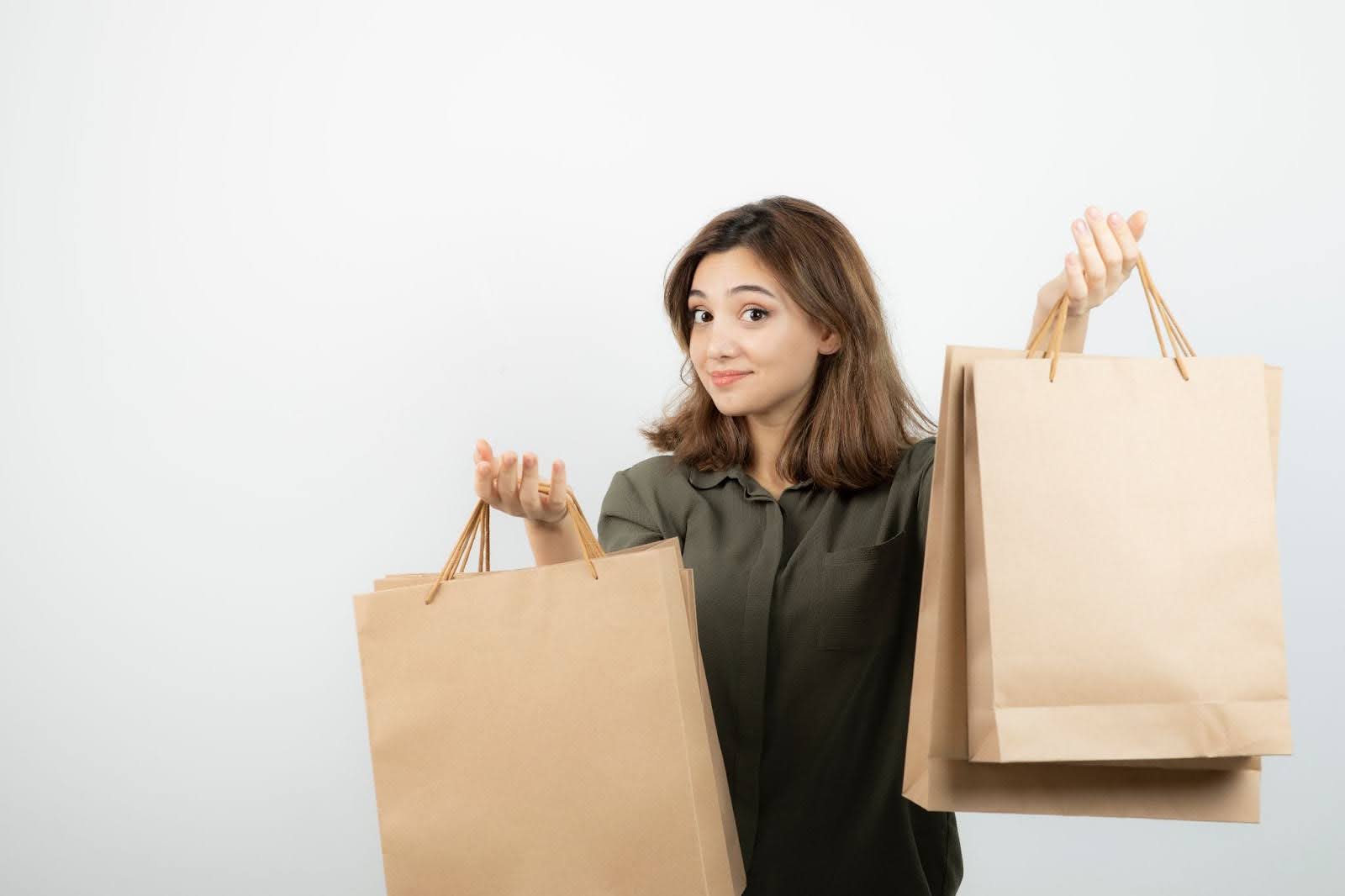 Smiling young woman holding eco-friendly brown paper shopping bags against white background – promoting sustainable packaging